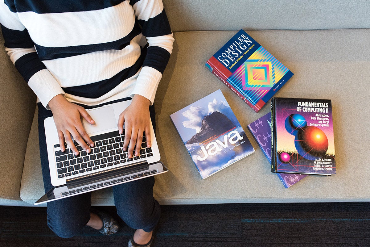 A woman using a laptop, surrounded by books on computing / programming / coding / development / Java