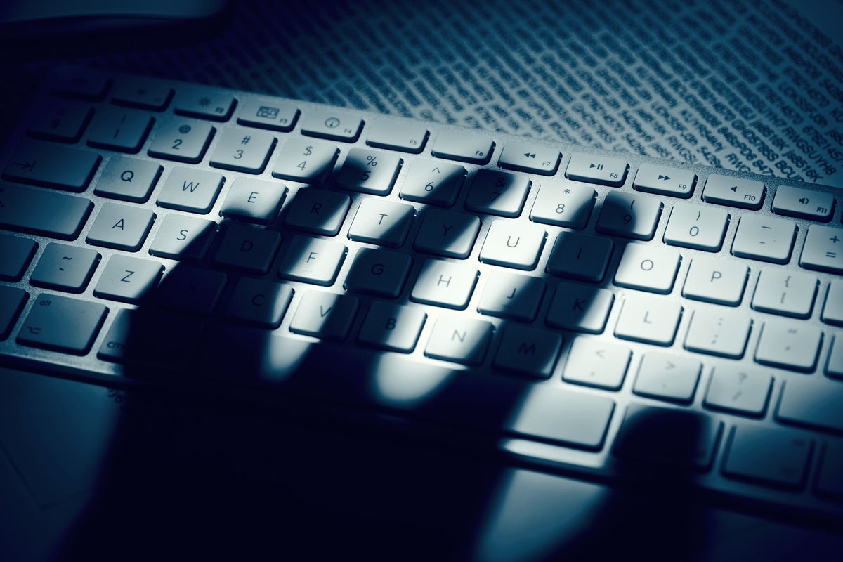 The shadow of hand unsettlingly hovers over a keyboard.